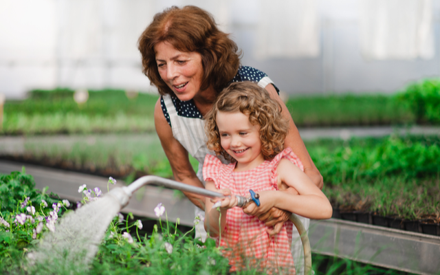 woman and young girl smiling and watering plants together.