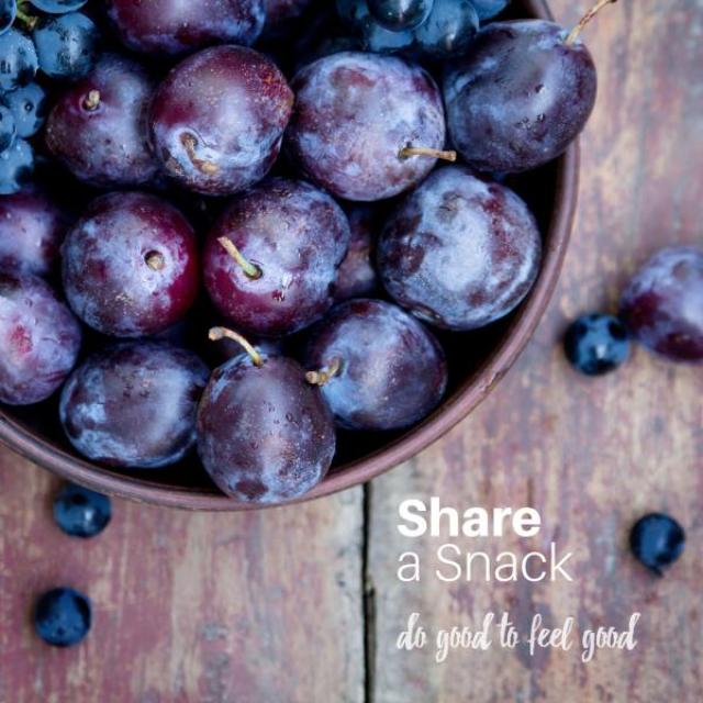 A bowl of purple grapes sits on a wooden table. The text "Share a snack. Do good to feel good." is overlaid in the corner. 
